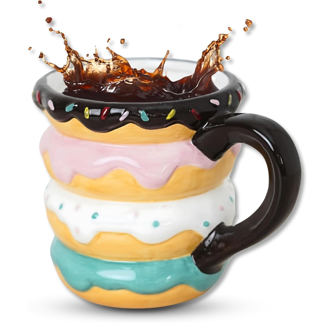 Donut-shaped ceramic mug with colorful frosting layers and a chocolate glaze rim, featuring a splash of coffee, and a black handle.