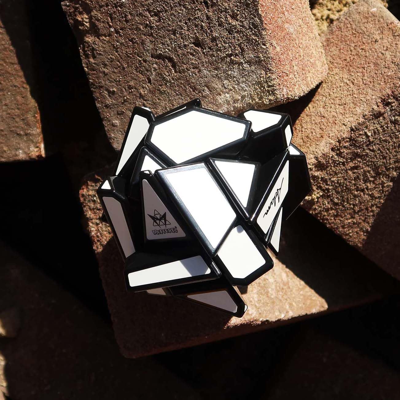 Scrambled Meffert’s Ghost Cube with black geometric edges and white stickers, resting on stacked rough bricks.