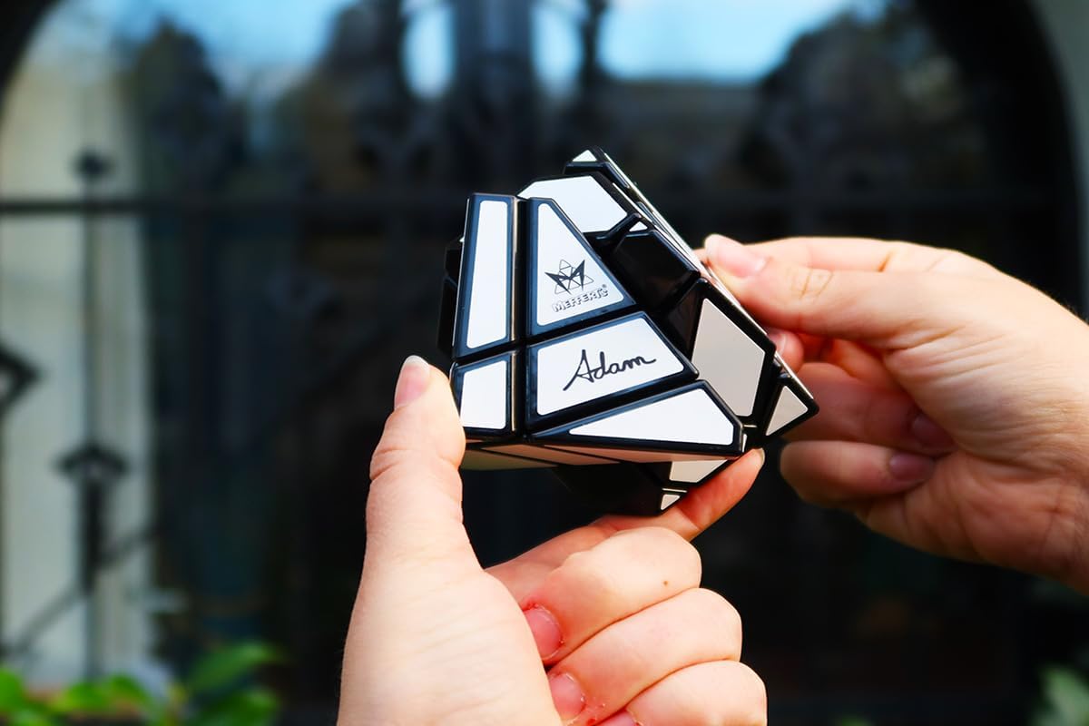 Two hands holding a partially twisted Meffert’s Ghost Cube, a black and white shape-shifting puzzle, against a blurred background.