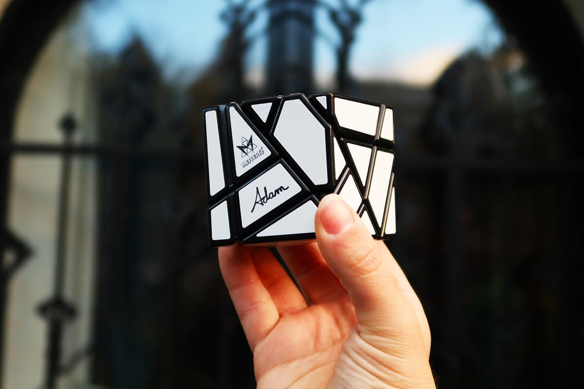 A hand holding a solved Meffert’s Ghost Cube, a black and silver shape-shifting puzzle, against a blurred outdoor background.