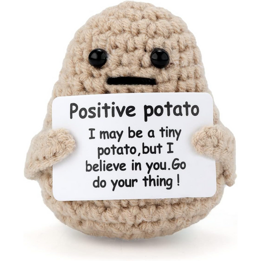 A small, crocheted plush toy shaped like a potato with black button eyes and a simple black stitched mouth. The plush toy is holding a white card with a motivational message that reads: "Positive potato. I may be a tiny potato, but I believe in you. Go do your thing!" The toy has short arms and a round, soft appearance, giving it a cute and encouraging vibe.