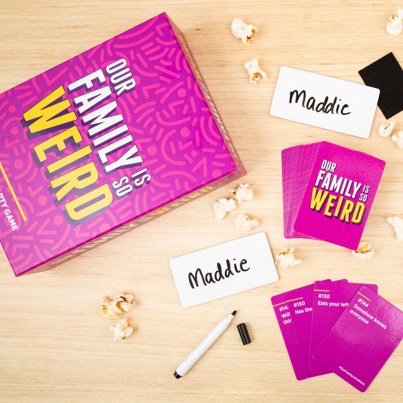 "Our Family Is So Weird" game setup, pink cards, name tags, markers, popcorn.