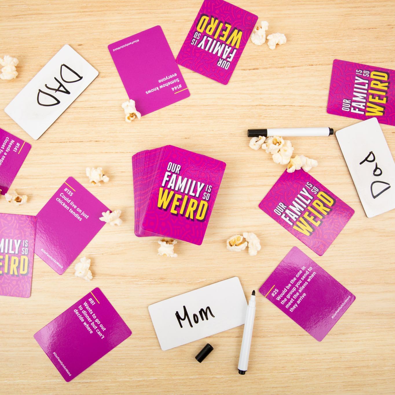 "Our Family Is So Weird" game, pink cards, name tags, markers, popcorn on table.