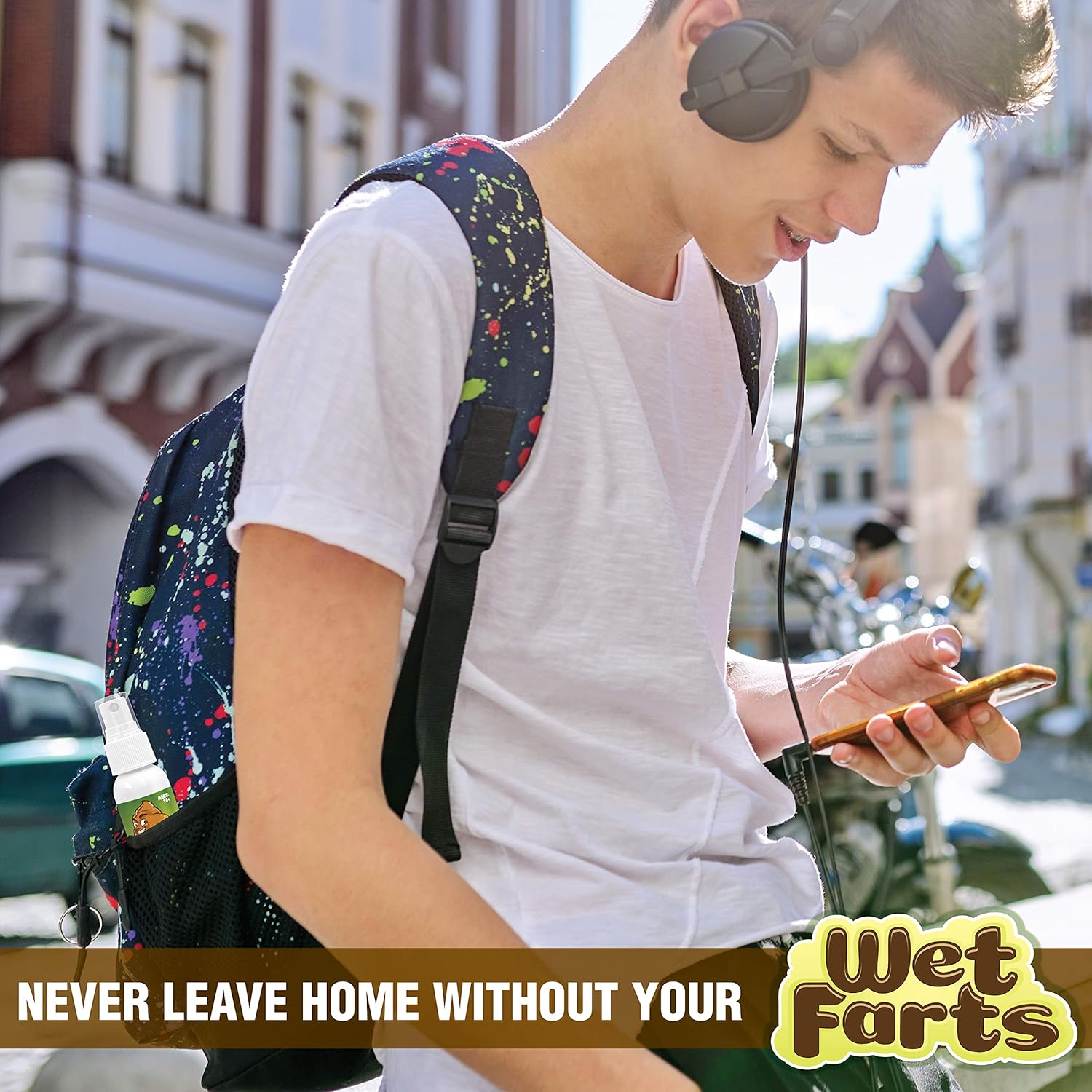 Young man with headphones and backpack carrying a "Wet Farts" spray bottle by Laughing Smith, using his phone on a city street. Text: "Never Leave Home Without Your Wet Farts".