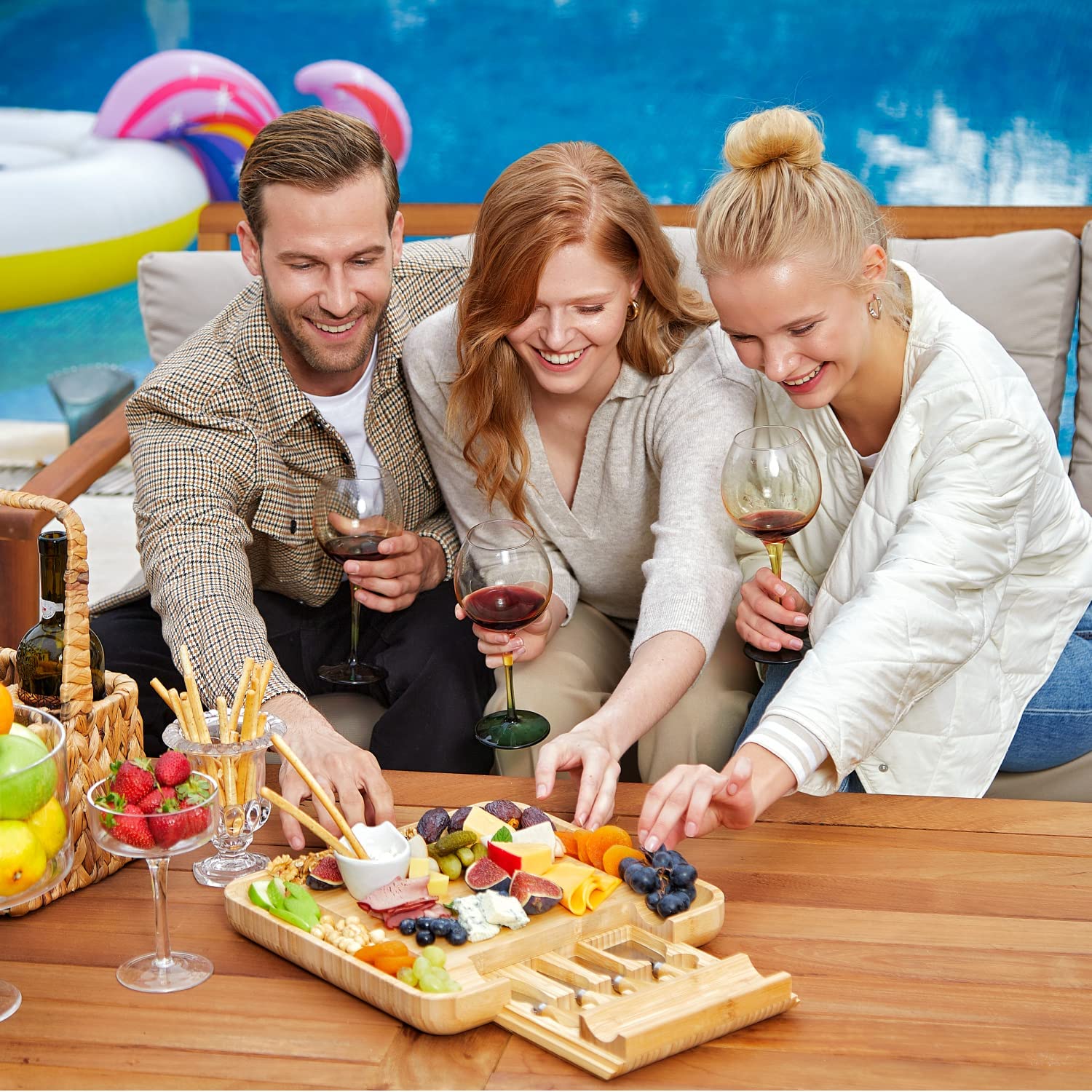 Two women and a man are grabbing some cheese and fruits off a cheese board and knife set with slide-out cutlery drawer